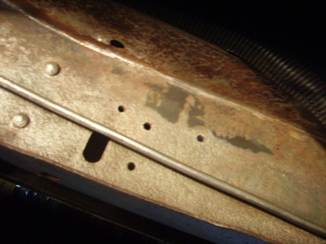 Close-up of rusted metal frame showing rivets, small holes, and a metal rod