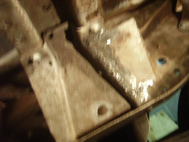 Underside of a vehicle showing frame rails and suspension parts. Some areas appear to have been welded
