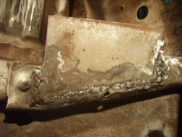 Close-up of metal repair with rough welds on a vehicle frame.