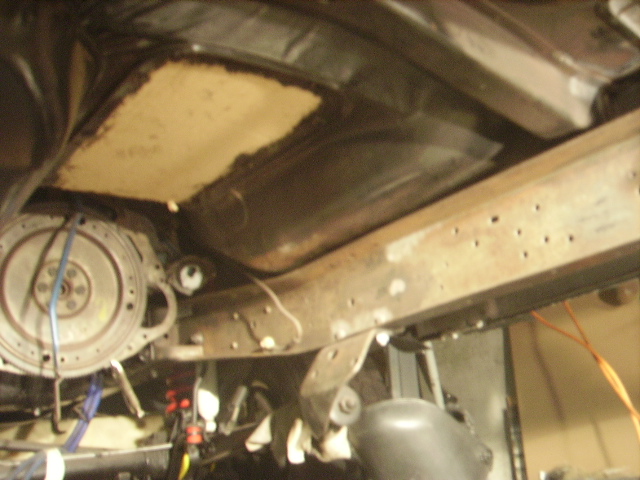 Underside of a vehicle showing frame, flywheel, and transmission housing.