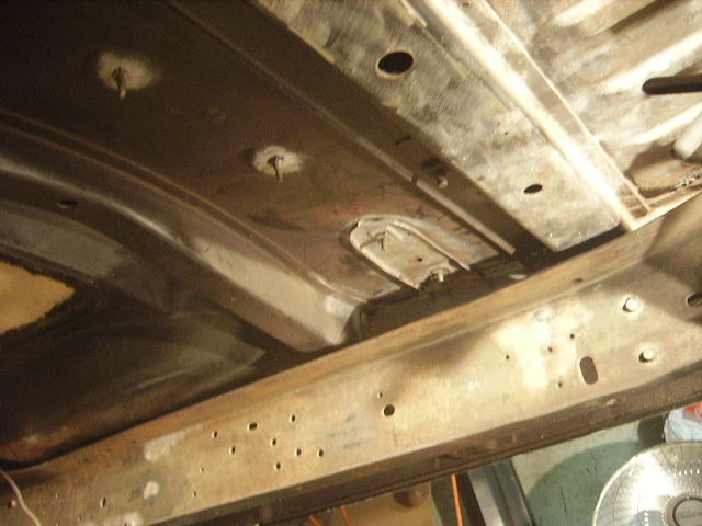 Underside of a vehicle chassis with rust and structural components.