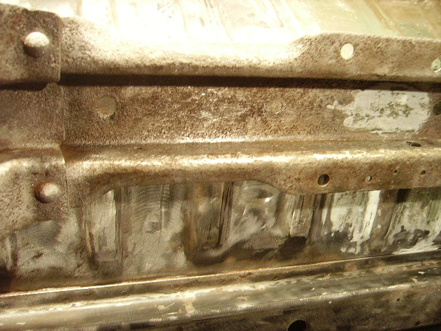Close-up of rusted vehicle frame underside with some cleaned areas.