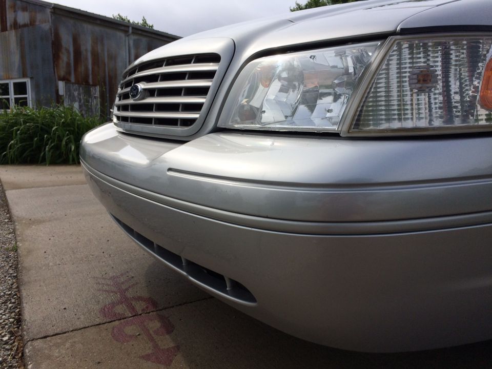 Silver Ford Crown Victoria front grille and headlight, low angle.