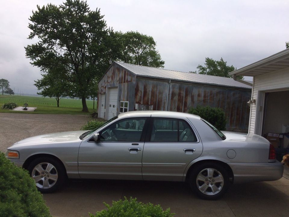 Silver 2003 Ford Crown Victoria sedan parked in front of a metal garage.