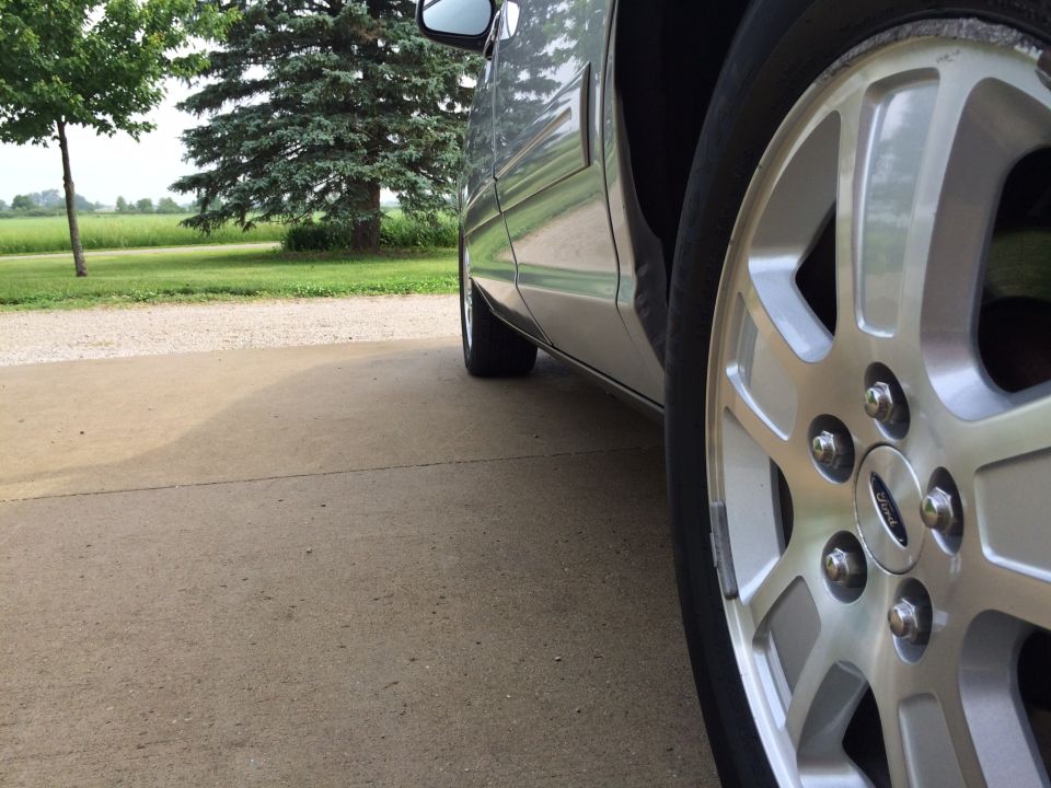 Silver sedan's front passenger wheel and fender, parked on a concrete driveway.
