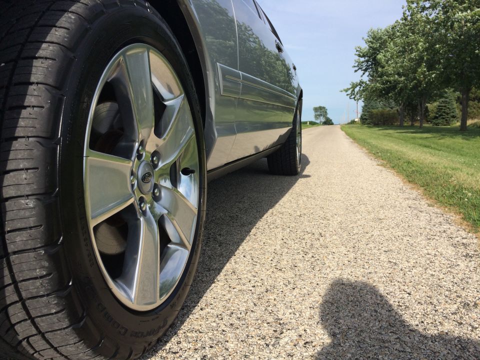 Close-up of a car's front wheel and side panel on a gravel road