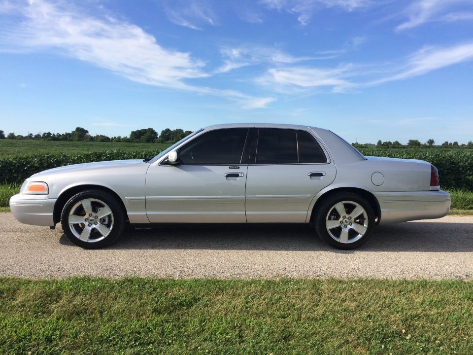 Silver 2003 Ford Crown Victoria parked on a gravel road with a field behind it
