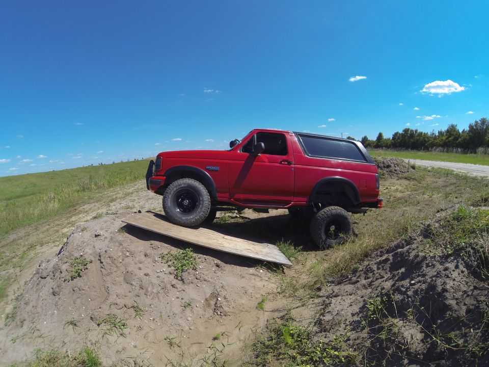 Red Ford Bronco on a dirt mound with a wooden plank under the front tire.