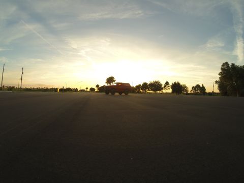 1995 Ford Bronco - A red 1995 Ford Bronco is parked on an asphalt surface during sunset. The vehicle is viewed from a low angle, with trees and utility poles…