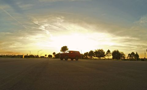 1995 Ford Bronco - A red two-door SUV is parked on asphalt during sunset, with palm trees and other foliage in the background.