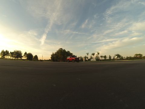 1995 Ford Bronco - A red 1995 Ford Bronco is parked in an asphalt lot with trees and palm trees in the background under a partly cloudy sky at sunset.