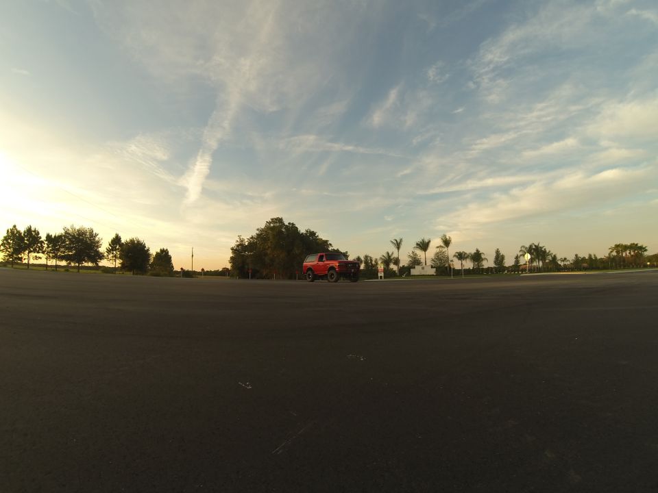 1995 Ford Bronco parked in an asphalt lot with trees and palm trees in the background at sunset.