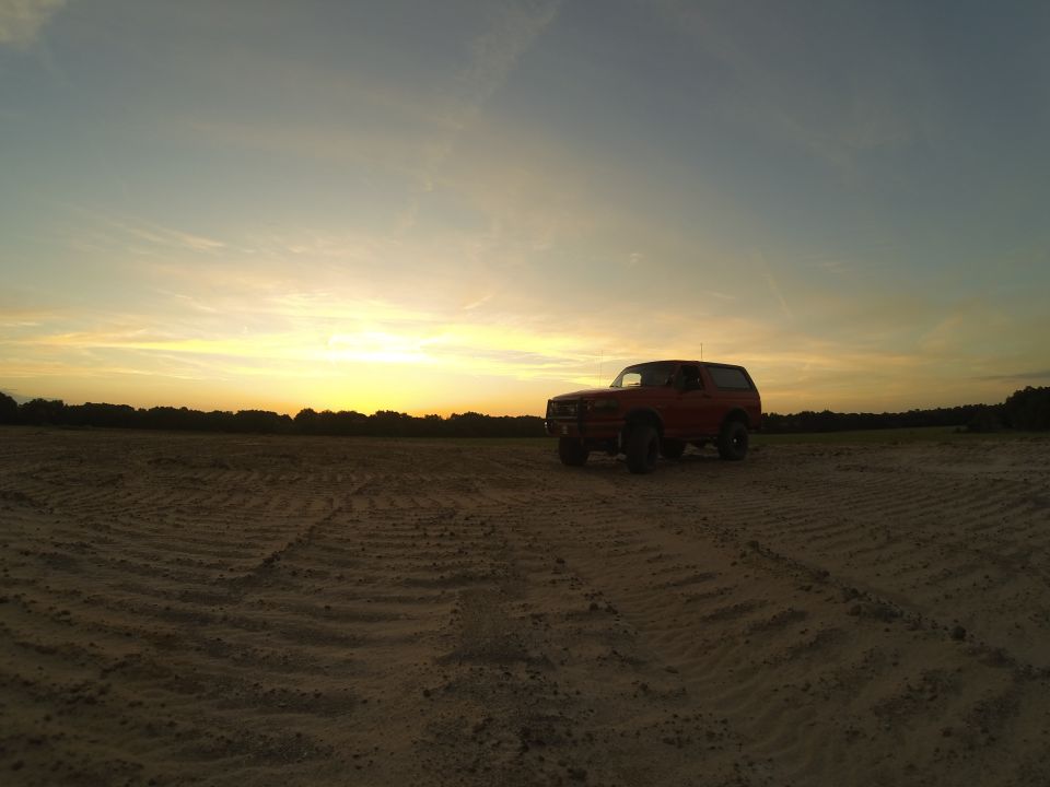 Red 1995 Ford Bronco parked in a dirt field at sunset.
