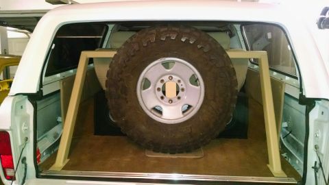 1979 Ford Bronco - The rear cargo area of a white Ford Bronco features a large spare tire mounted on a custom metal rack. The spare tire is positioned in fron…
