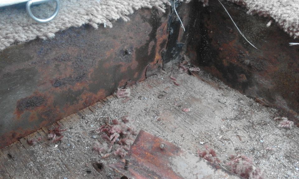 Rusted metal interior of a vehicle chassis with wood floor and debris.