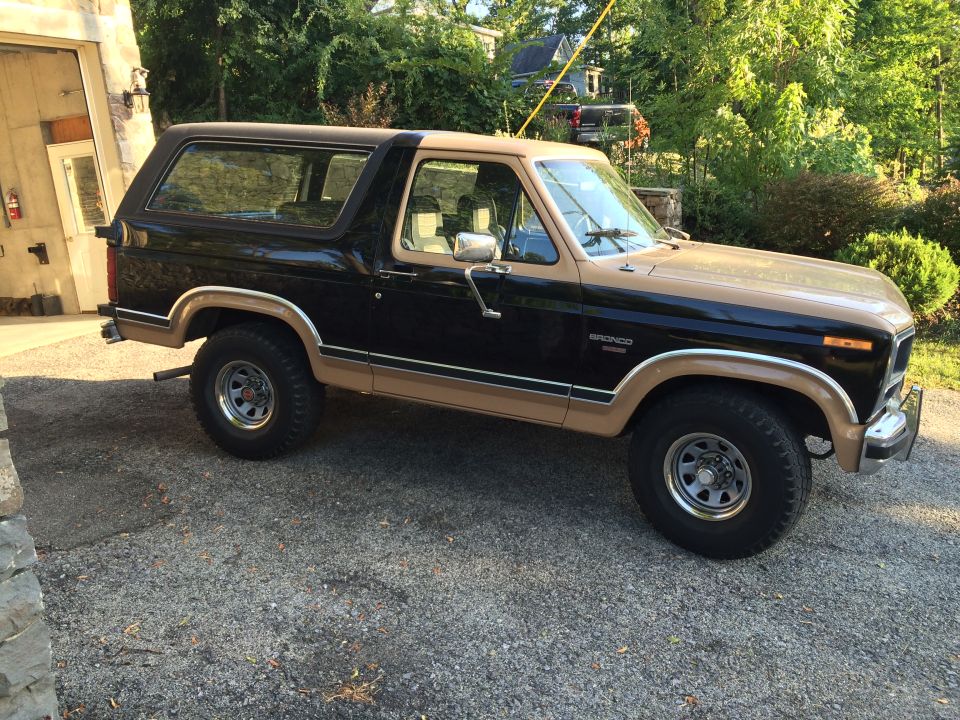 1983 Ford Bronco, black and tan, parked outside a garage.