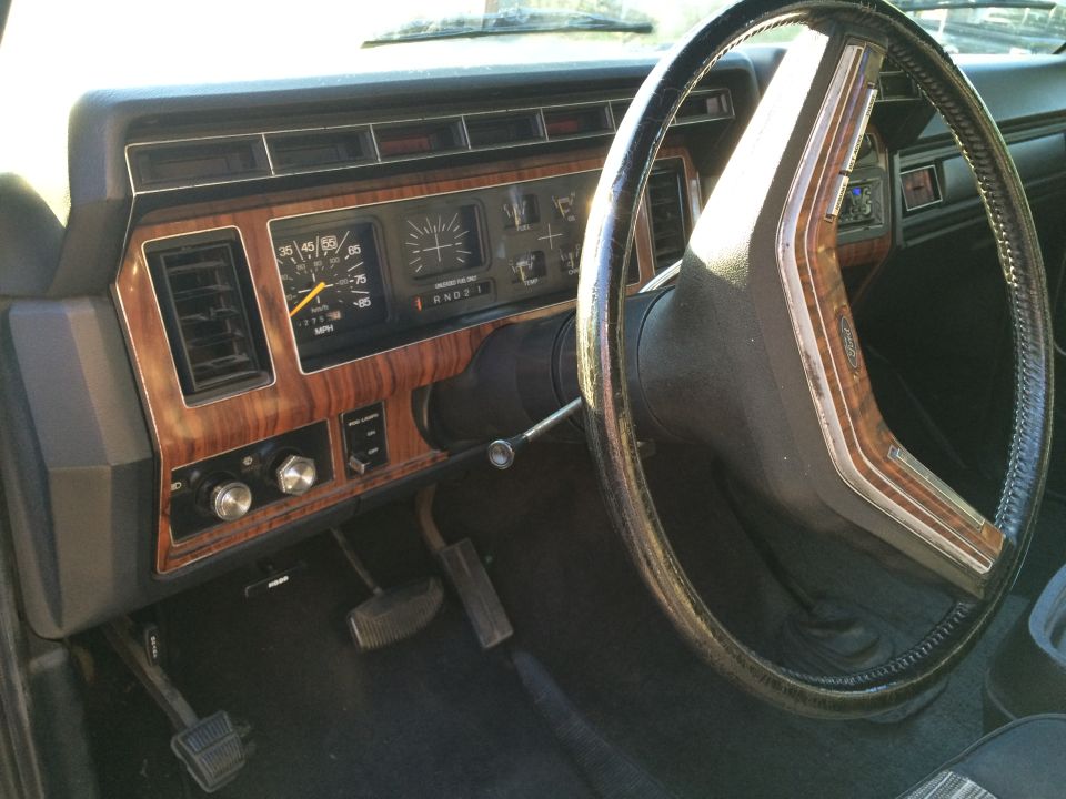 Interior of a vintage Ford Bronco dashboard with wood grain, gauges, and steering wheel.
