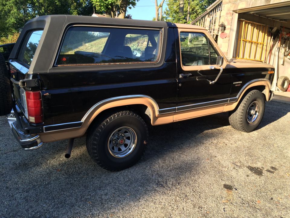 1980s black and tan Ford Bronco, rear driver's side view, spare tire on back