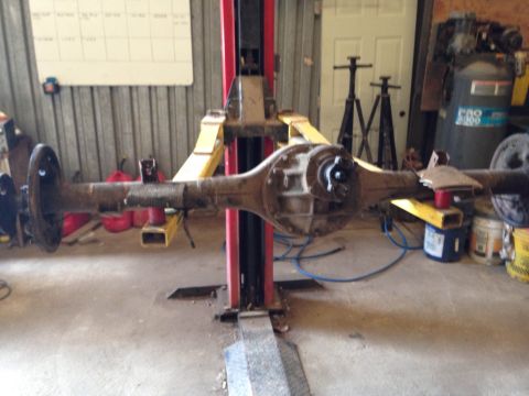 1979 Ford Bronco - A rear axle assembly, likely from a 1979 Ford Bronco, is supported by a vehicle lift in a garage setting. The assembly shows signs of wear…
