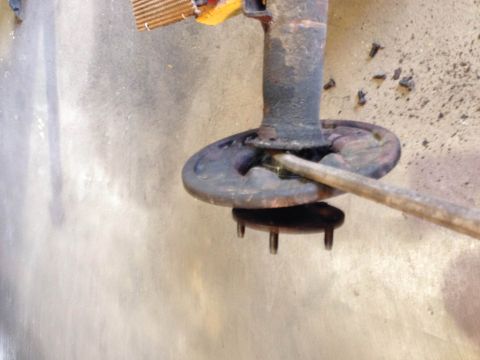 1979 Ford Bronco - A close-up view of a rusty wheel hub assembly being worked on with a pry bar, with several screws scattered on the concrete floor.