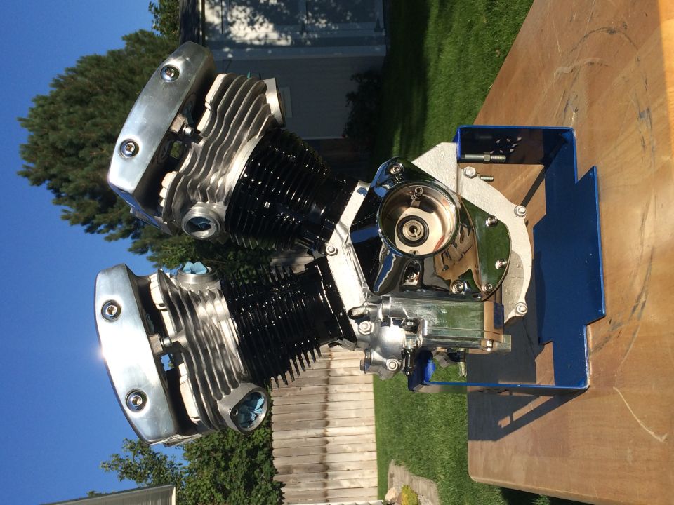 Polished V-twin motorcycle engine with black cylinders on a blue stand.
