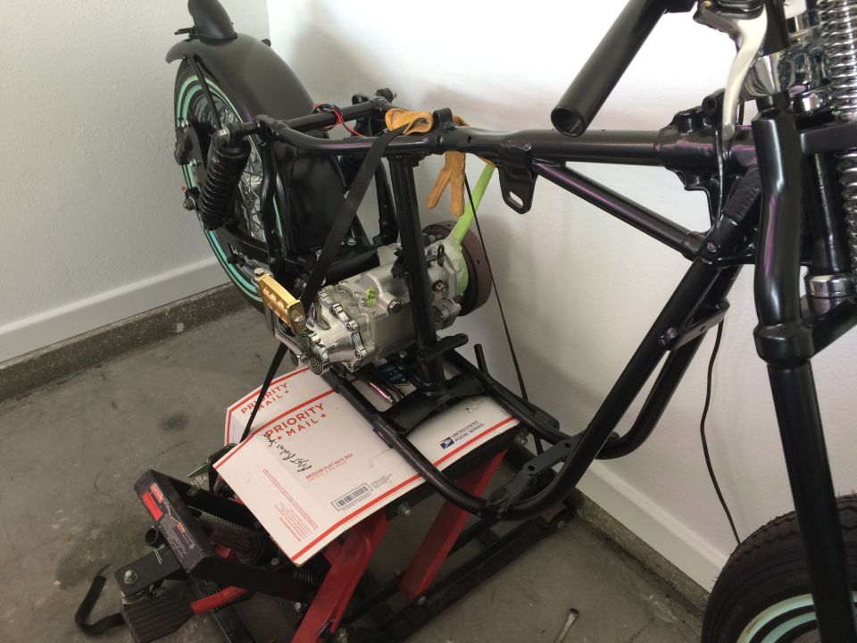 Motorcycle frame with engine installed on a lift, rear wheel and fender visible.