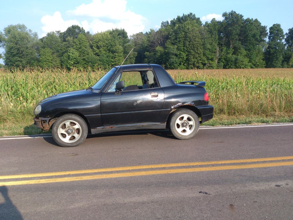 Black convertible sports car with aftermarket wheels parked by a cornfield.