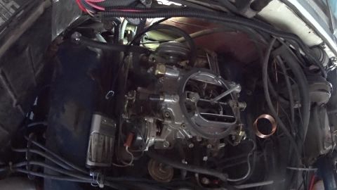 1978 Ford Bronco - The engine bay of a classic Ford Bronco shows a carburetor and various hoses and wiring. A silver battery charger is mounted to the inner f…