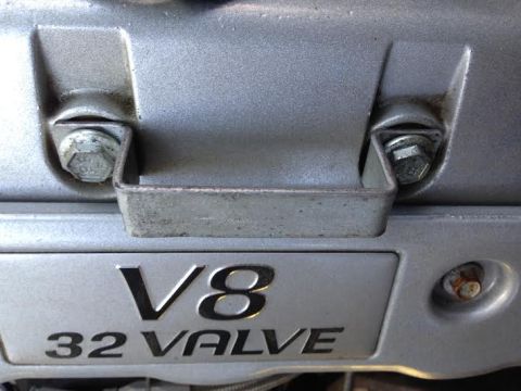2004 Ford Crown Victoria - A close-up view of a silver V8 32 valve engine cover with two bolts securing a metal bracket. The engine cover has visible text indicating…