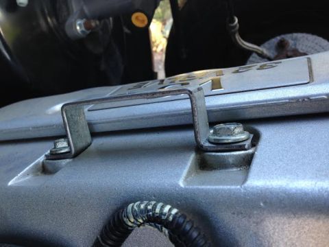 2004 Ford Crown Victoria - A close-up, angled shot shows a metal bracket secured by a bolt to the silver engine cover of a Ford Crown Victoria. The engine cover has r…
