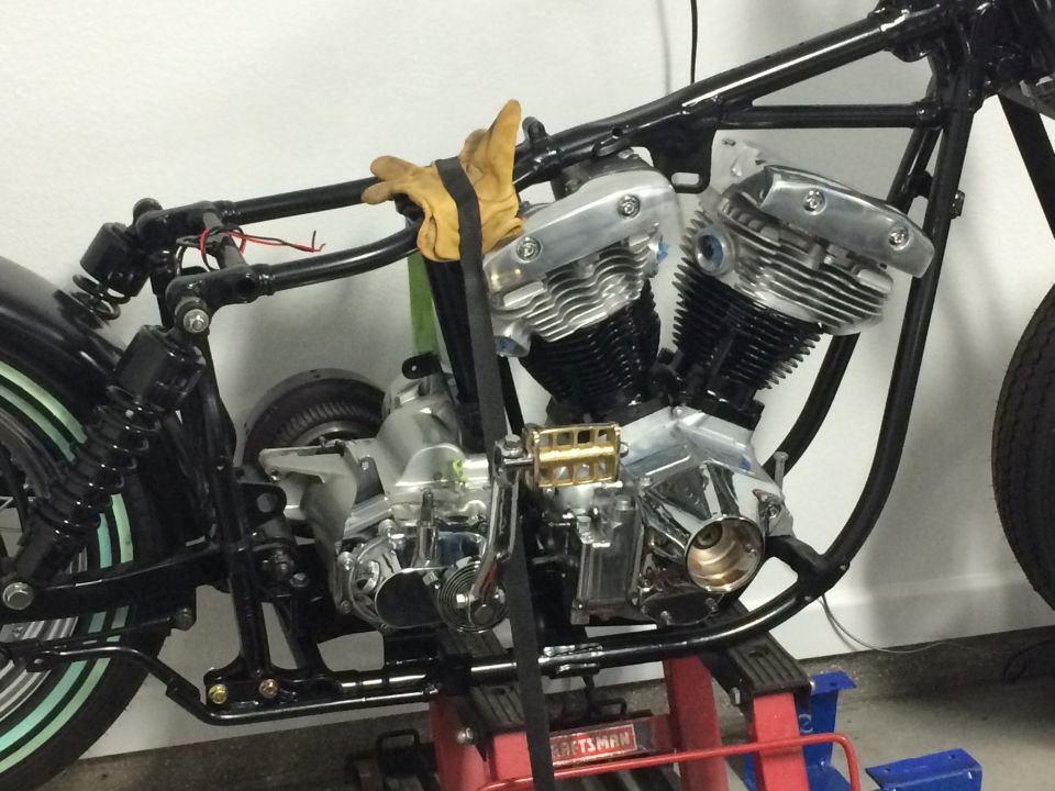 Motorcycle engine and frame on a stand with yellow gloves.