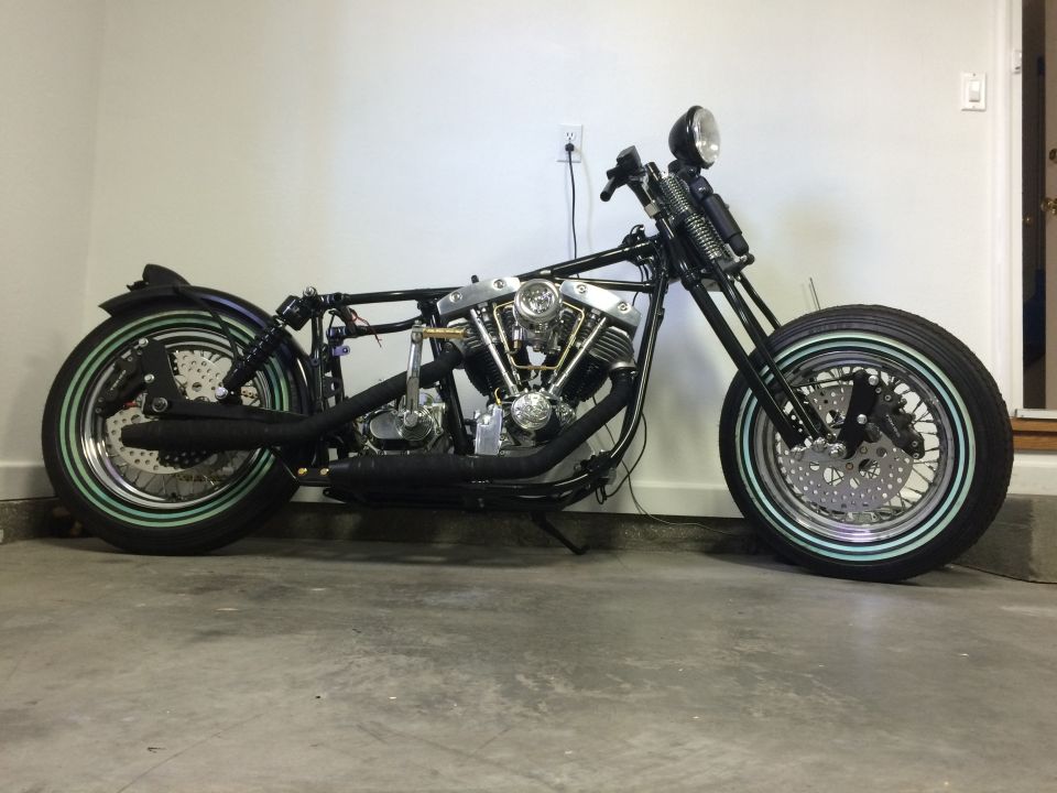 Custom motorcycle, black frame, engine, exhaust, and wheels with pinstripes, side view.