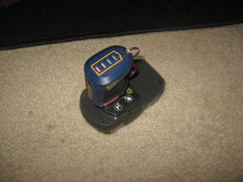 1994 Ford Bronco - A Ryobi ONE+ battery pack with a keychain attached is sitting on a black charging base. The battery pack has a charge indicator showing fou…