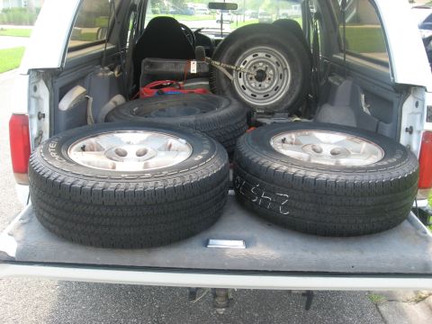 1994 Ford Bronco - The bed of a white Ford Bronco is filled with four tires. Two tires are stacked in the front, and two are laid flat in the back.