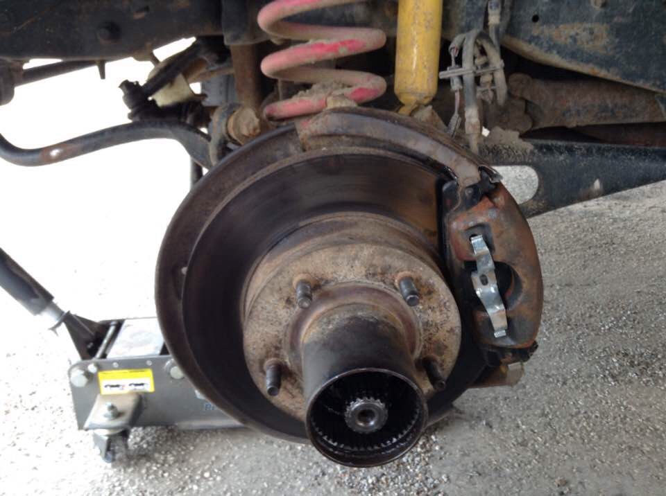 Close-up of a vehicle's front brake assembly with rotor, caliper, and hub, on a jack.