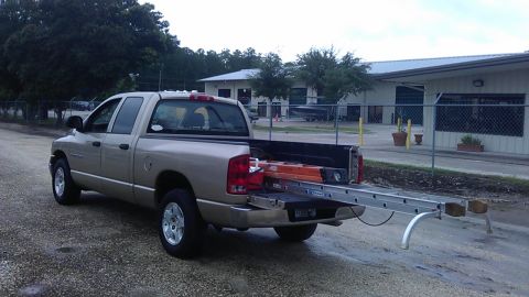 1994 Ford Bronco - A tan pickup truck is parked on a gravel surface with a ladder rack extending from the bed. The truck bed contains an orange ladder and oth…