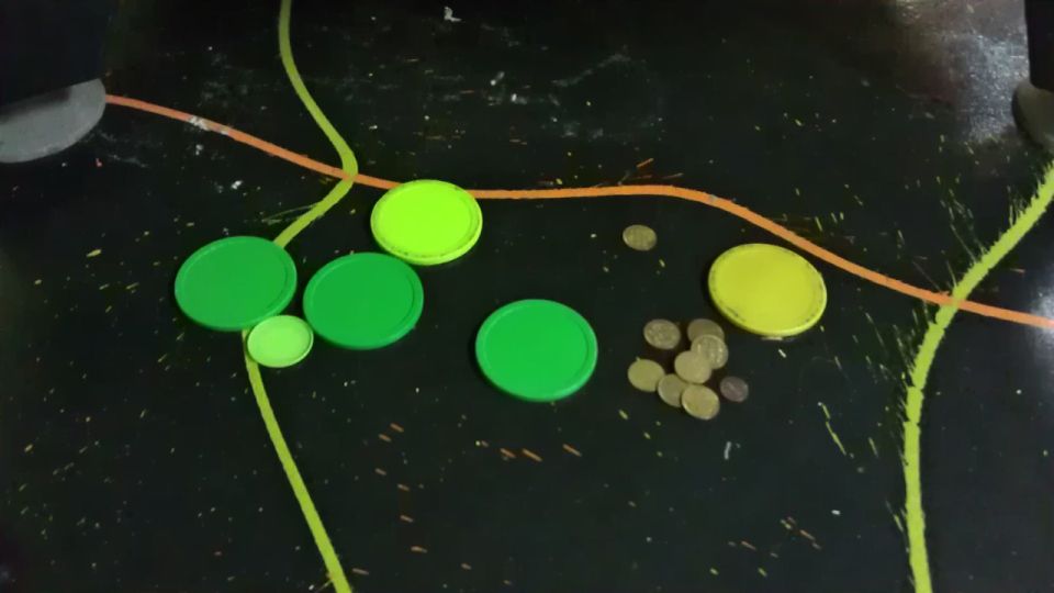 Green and yellow bottle caps and coins on a black surface with painted lines.