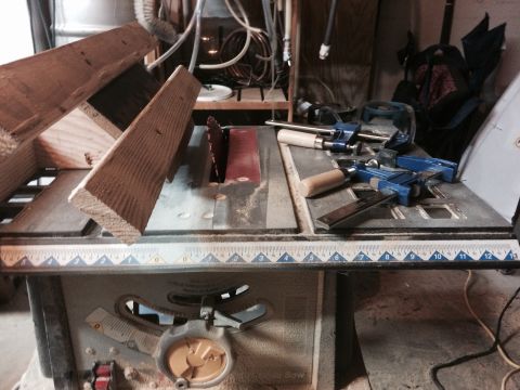 1979 Ford Bronco - A table saw is set up in a workshop with various tools and lumber. A piece of wood is positioned above the saw blade, and two blue clamp to…