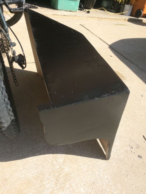 1979 Ford Bronco - A black, angled, boat-like object is shown outdoors on a concrete surface, next to a bicycle's rear wheel and chain. The object appears to…