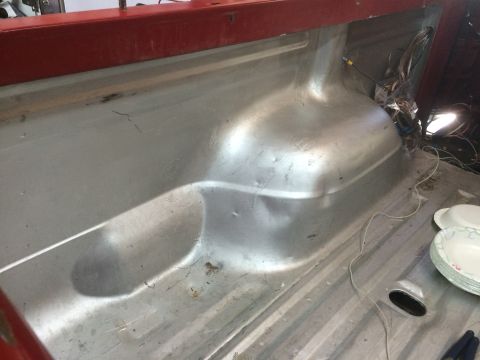 1979 Ford Bronco - The interior of a vehicle's bed or cargo area shows a silver metal floor with visible wheel well humps and wiring. A red metal bar runs alo…