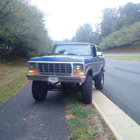 1978 Ford Bronco - A lifted blue 1978 Ford Bronco is parked on the side of a road with trees lining the left side of the frame. The vehicle has large off-road…