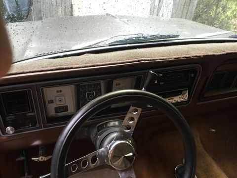 1978 Ford Bronco - The interior of a classic Ford Bronco shows the dashboard with a steering wheel, radio, and gauges. The windshield is visible with water dr…