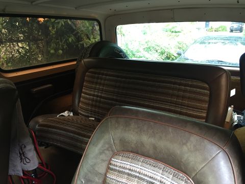 1978 Ford Bronco - Interior view of a classic Ford Bronco showing the rear bench seat with a plaid fabric insert and brown leatherette bolsters. A spare tire…