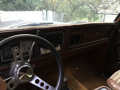 1978 Ford Bronco - The interior of a vintage Ford Bronco shows the dashboard, steering wheel, and driver's side floor. The dashboard features wood grain trim…