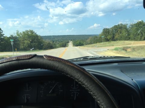1993 Ford Bronco - View from the driver's seat of a 1993 Ford Bronco, looking out over a two-lane road that winds through a hilly, tree-covered landscape unde…