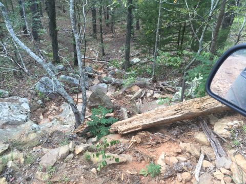 1993 Ford Bronco - A side mirror of a vehicle reflects a rocky, wooded trail. The vehicle appears to be an off-road SUV, possibly a 1993 Ford Bronco, navigati…