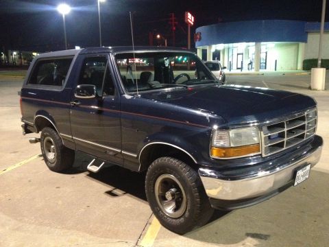 1993 Ford Bronco - A dark blue Ford Bronco is parked at night in a parking lot in front of a building. The vehicle is viewed from the front three-quarter angl…