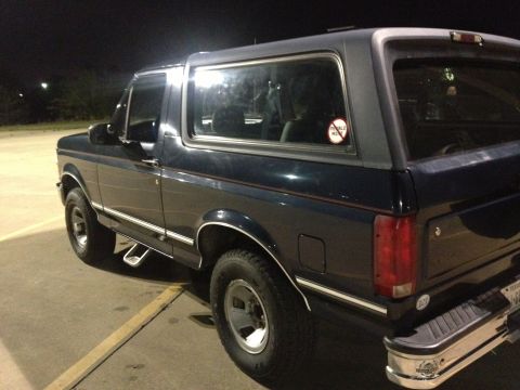 1993 Ford Bronco - The right side of a dark blue Ford Bronco is shown parked on pavement at night. A sticker on the rear passenger window reads "Pebble Beach".