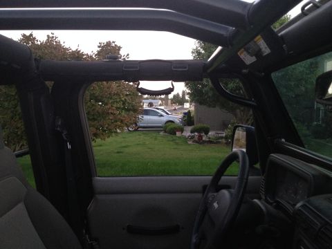 2005 Jeep Wrangler - View from inside a Jeep Wrangler looking out the driver's side window at a residential yard with a silver sedan parked in the driveway. The…