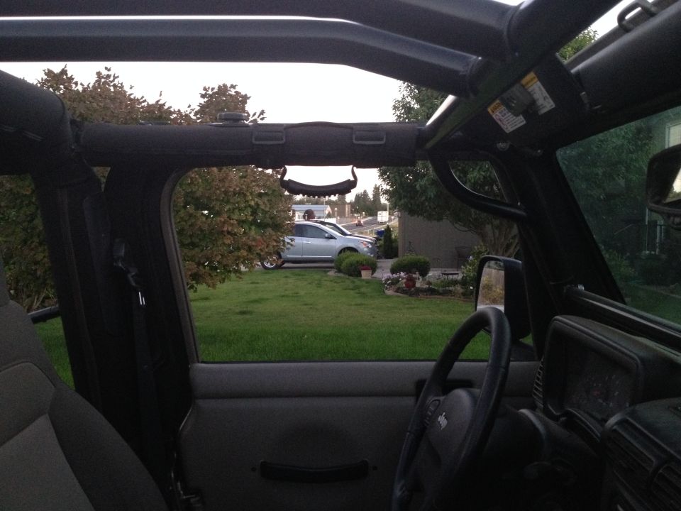 Interior view of a Jeep Wrangler showing the dashboard, steering wheel, and a silver sedan outside.